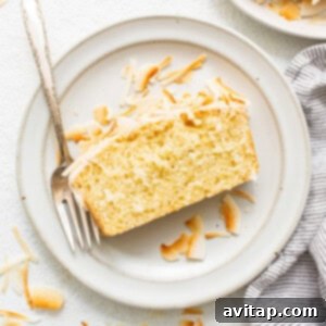 A beautifully glazed coconut loaf cake, adorned with toasted coconut flakes, presented on a plate and ready to be served.