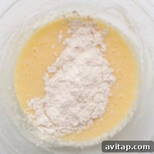 A spatula scraping down the sides of a mixing bowl, ensuring thorough combination of wet and dry ingredients for the coconut loaf cake batter.