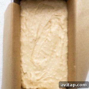 A golden-brown coconut cake baking perfectly in a loaf pan, centered on a white surface.