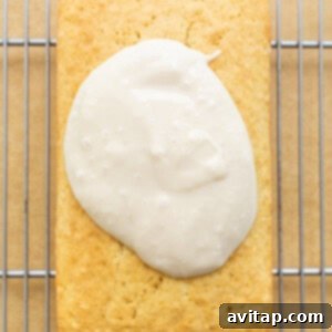 A freshly glazed coconut loaf cake resting on a cooling rack, with the white glaze dripping slightly down the sides.