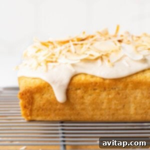 Close-up of shredded coconut and flakes being pressed onto the top of a freshly glazed coconut loaf cake, enhancing its tropical appeal.