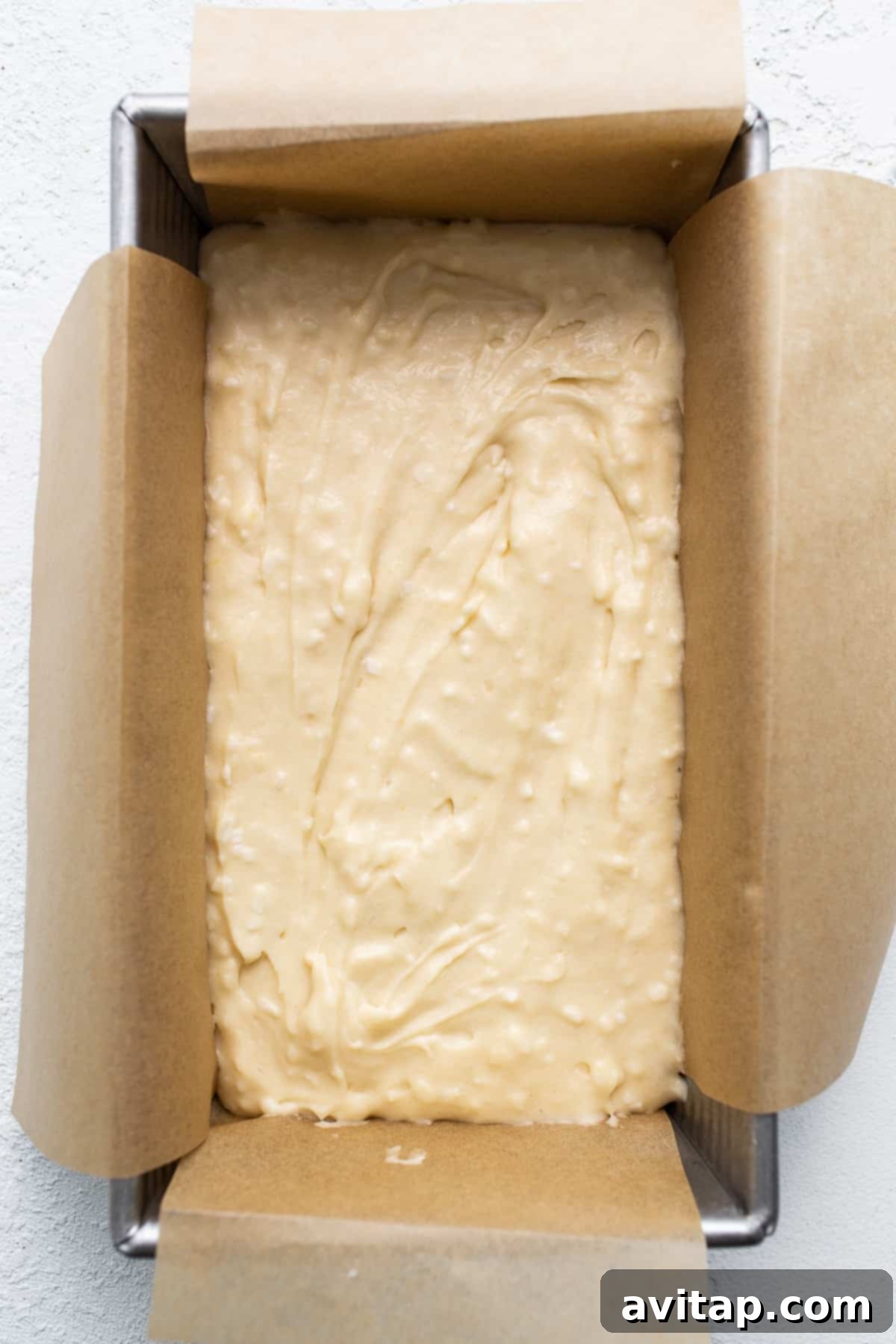Thick, creamy coconut loaf cake batter being poured into a parchment-lined loaf pan, ready for its journey into the oven.