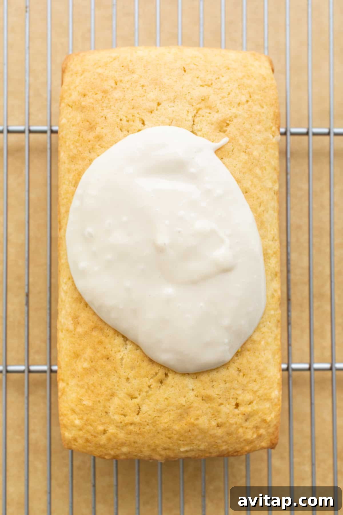 A close-up view of the luscious coconut glaze being drizzled over the baked coconut loaf cake, with toasted coconut pieces scattered on top.