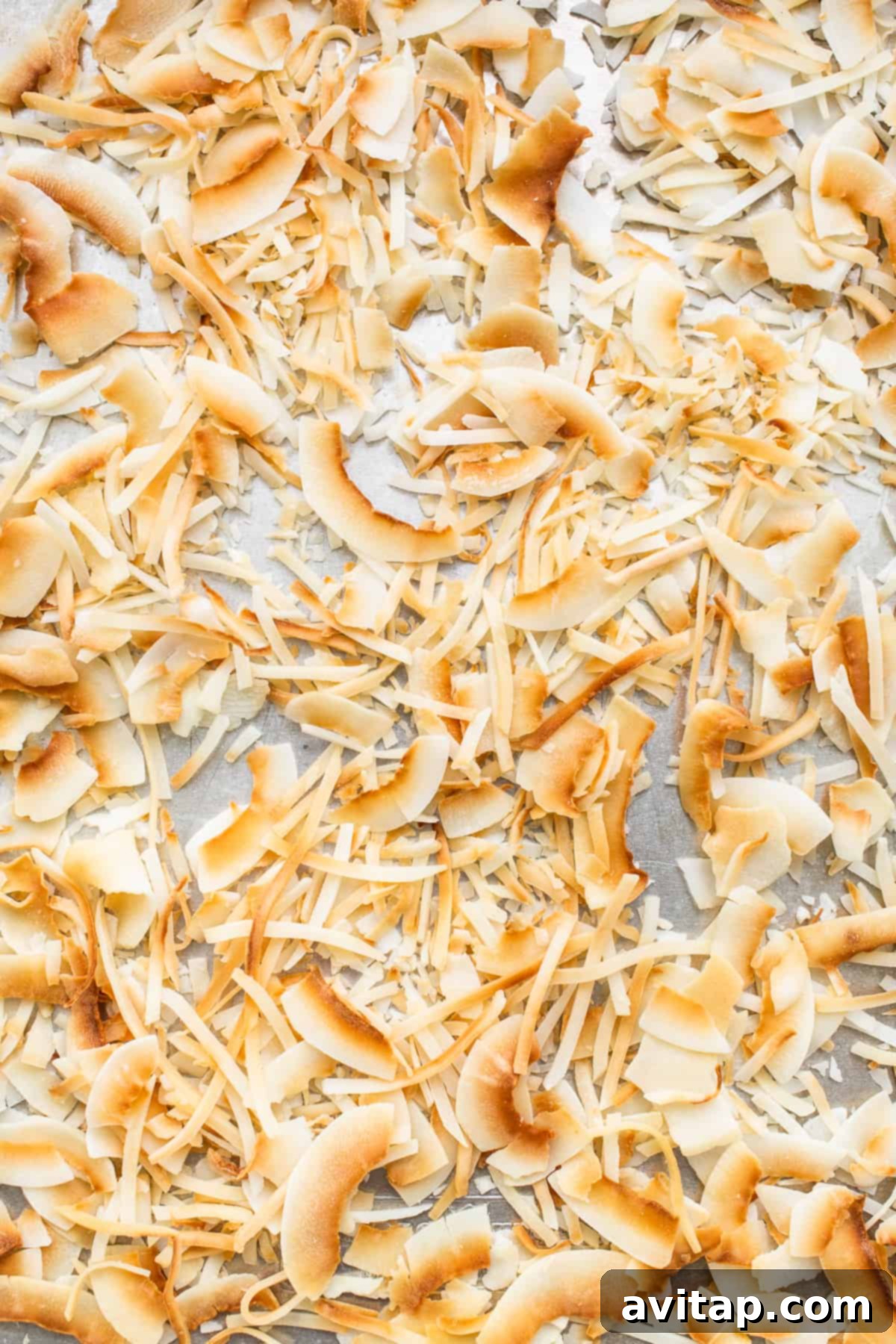 Toasted shredded coconut and coconut flakes spread on a baking sheet, golden brown and ready for topping the cake.