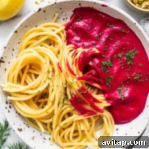 Spaghetti coated in a rich, pink beetroot sauce on a white plate, ready for garnishing.