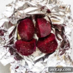 Beets wrapped in foil on a white surface, seasoned with oil, salt, and pepper.