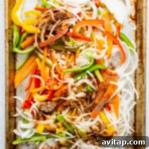 Sliced bell peppers and onions seasoned on a baking sheet, ready for the oven.