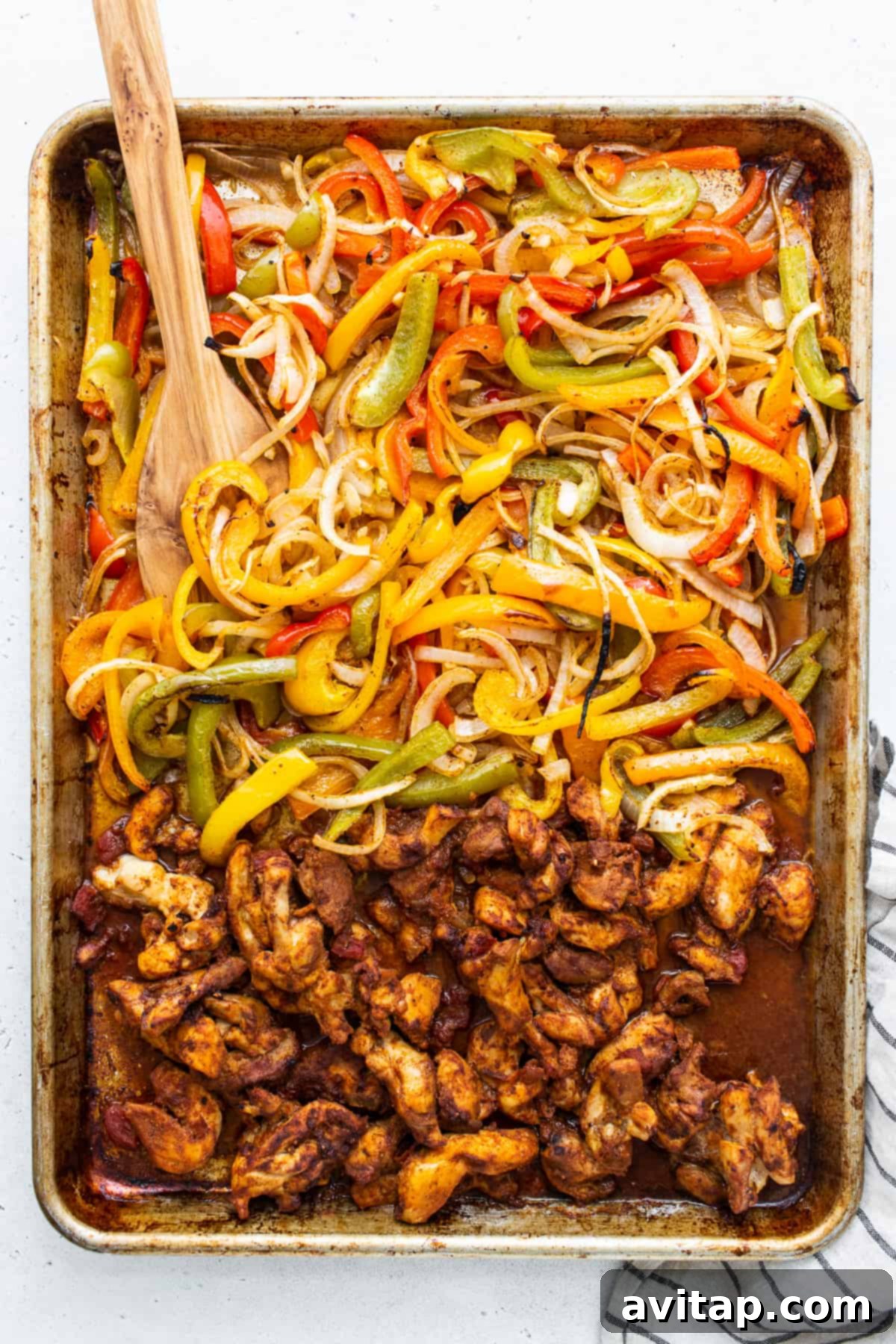 Cooked sheet pan chicken fajitas with caramelized peppers and onions directly on the baking sheet.