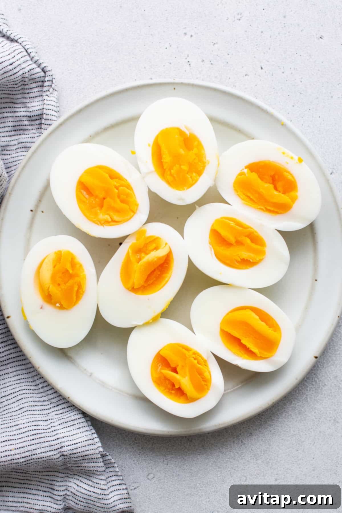 Two air fryer hard boiled eggs, halved to reveal perfect, vibrant yellow yolks, artfully arranged on a plate.