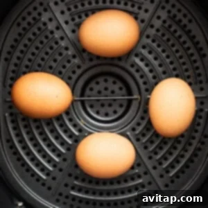 Three eggs are sitting in an air fryer basket, ready to be cooked.