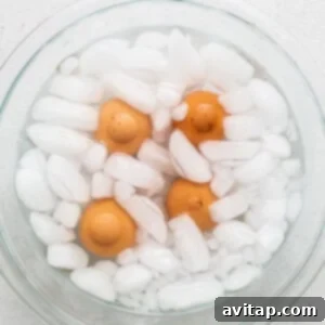A glass bowl filled with cooked eggs and ice cubes, in an ice water bath.