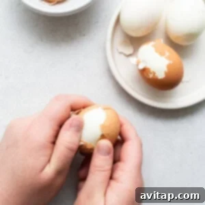 A person carefully peeling a hard boiled egg with a knife, revealing the smooth white surface.