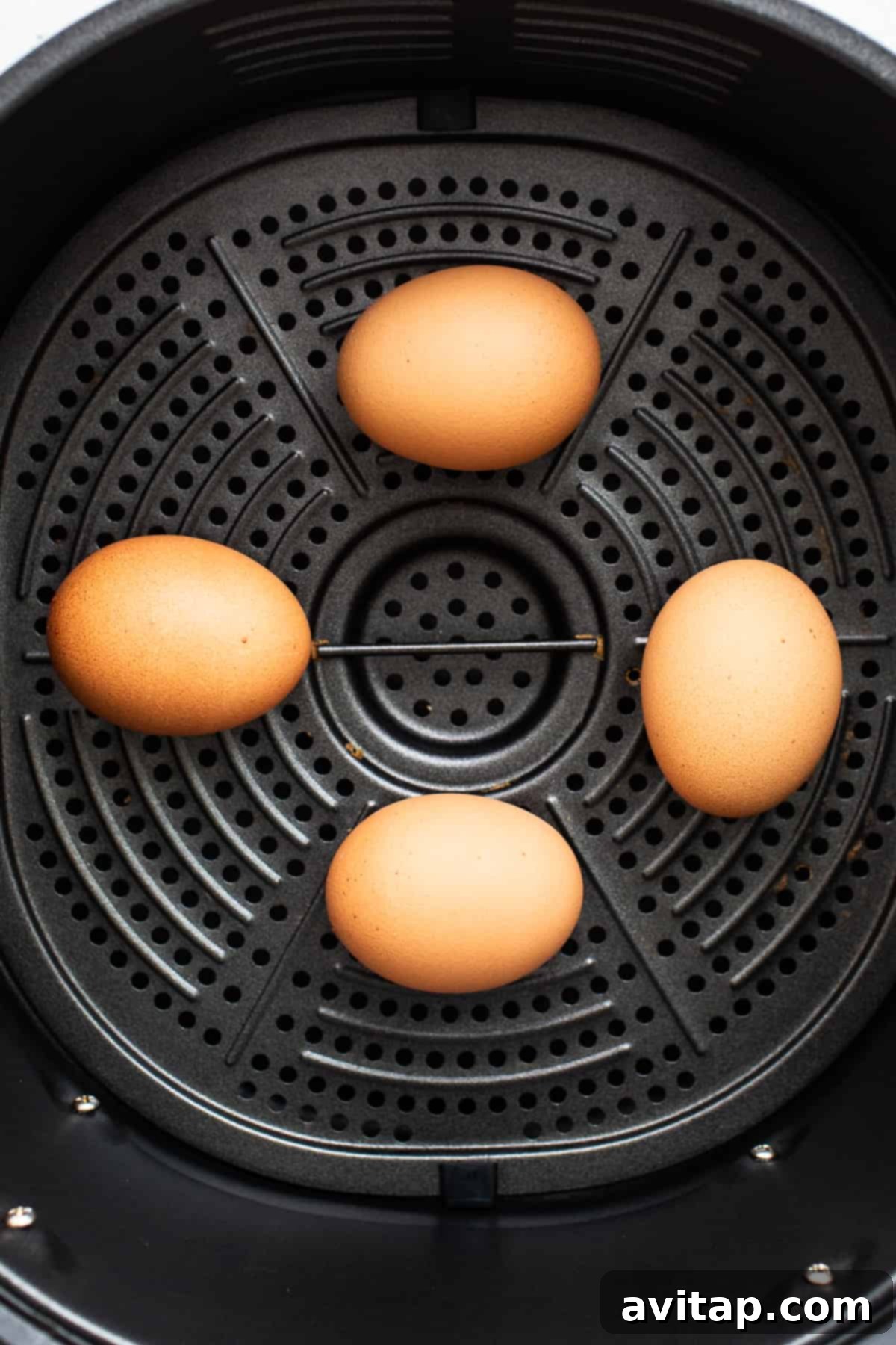 Four fresh eggs nestled in an air fryer basket, ready for cooking.