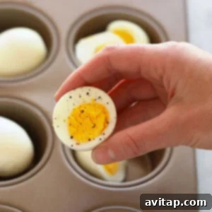 Hands carefully placing eggs into a muffin tin to prepare oven-baked hard boiled eggs.