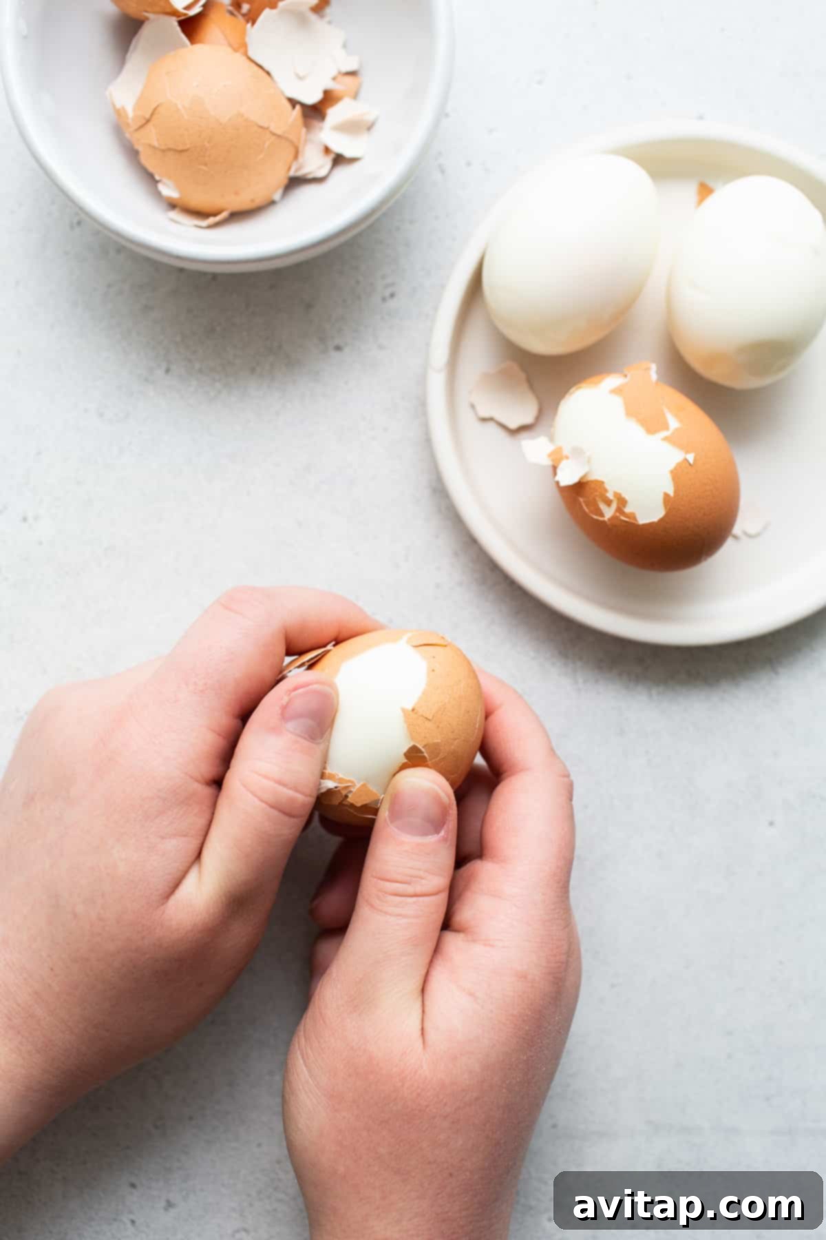 Hands carefully peeling a hard boiled egg, showing the smooth white surface beneath the shell.