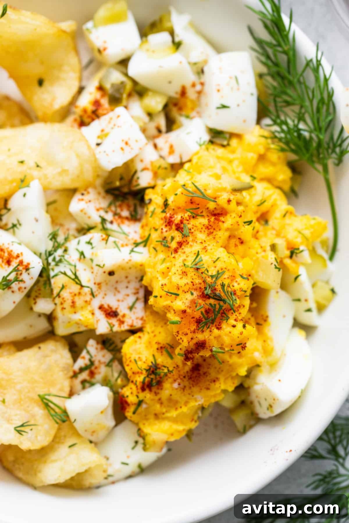 Deviled egg salad generously garnished with vibrant fresh dill and a sprinkle of paprika, presented in a pristine white serving bowl.