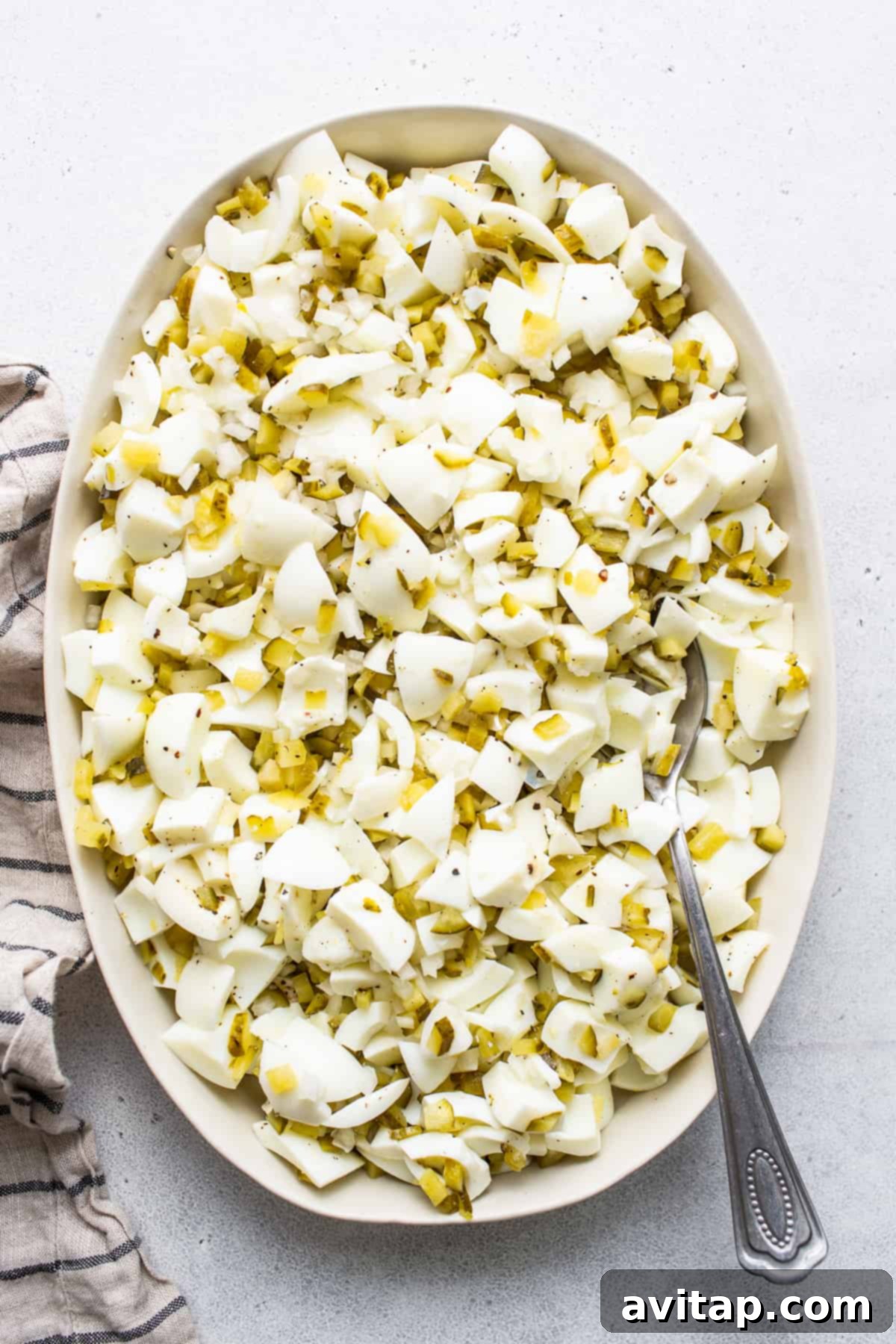 Finely chopped egg whites in a white mixing bowl with a spoon, perfectly prepared and ready for seasoning.