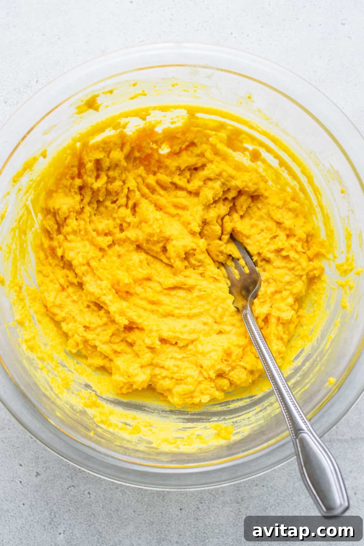 Creamy, perfectly mashed egg yolks blended with tangy condiments in a mixing bowl, with a fork resting inside.