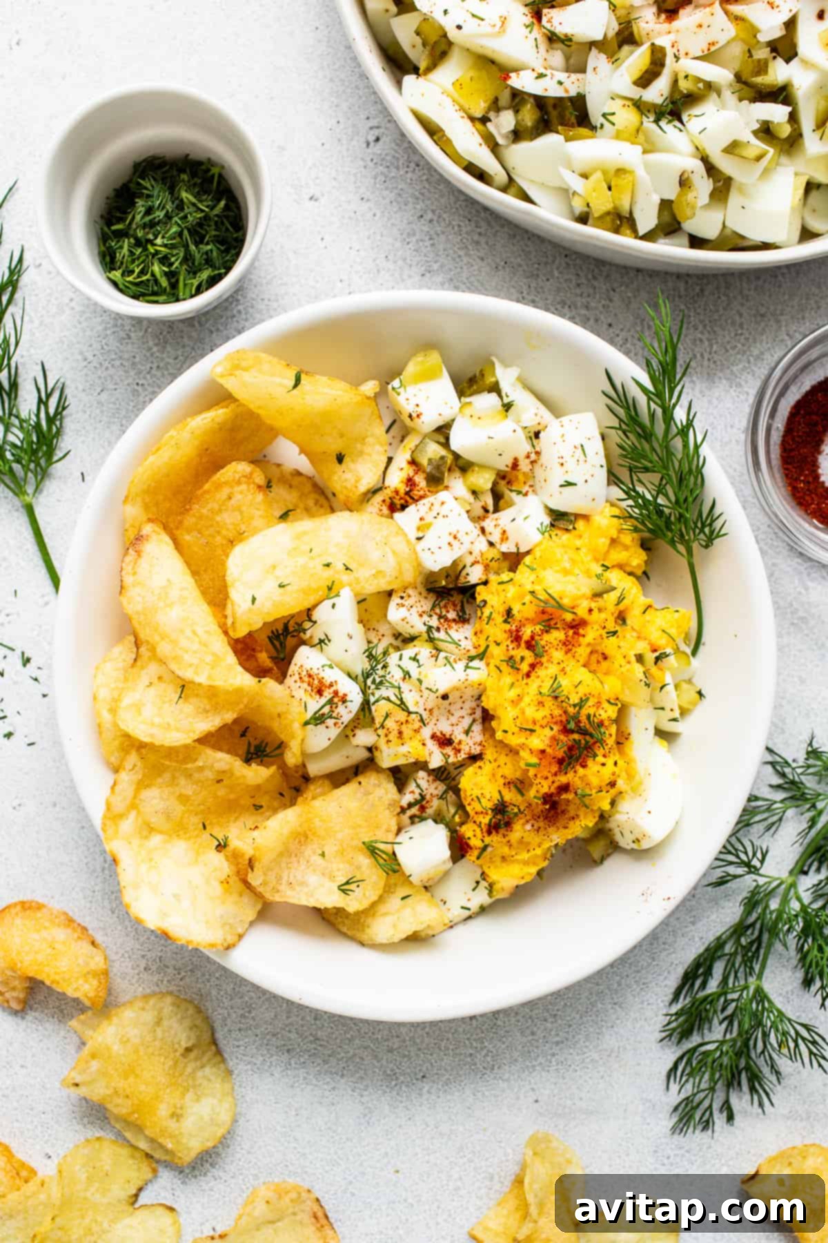 Deviled egg salad served in an elegant white bowl, surrounded by a scattering of golden, crispy potato chips for dipping.
