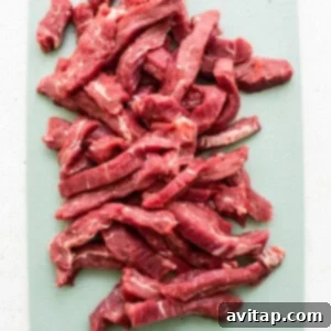 Thinly sliced beef strips on a cutting board, cut against the grain.
