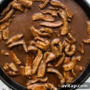 Beef cooking in the savory sauce in a large pan.