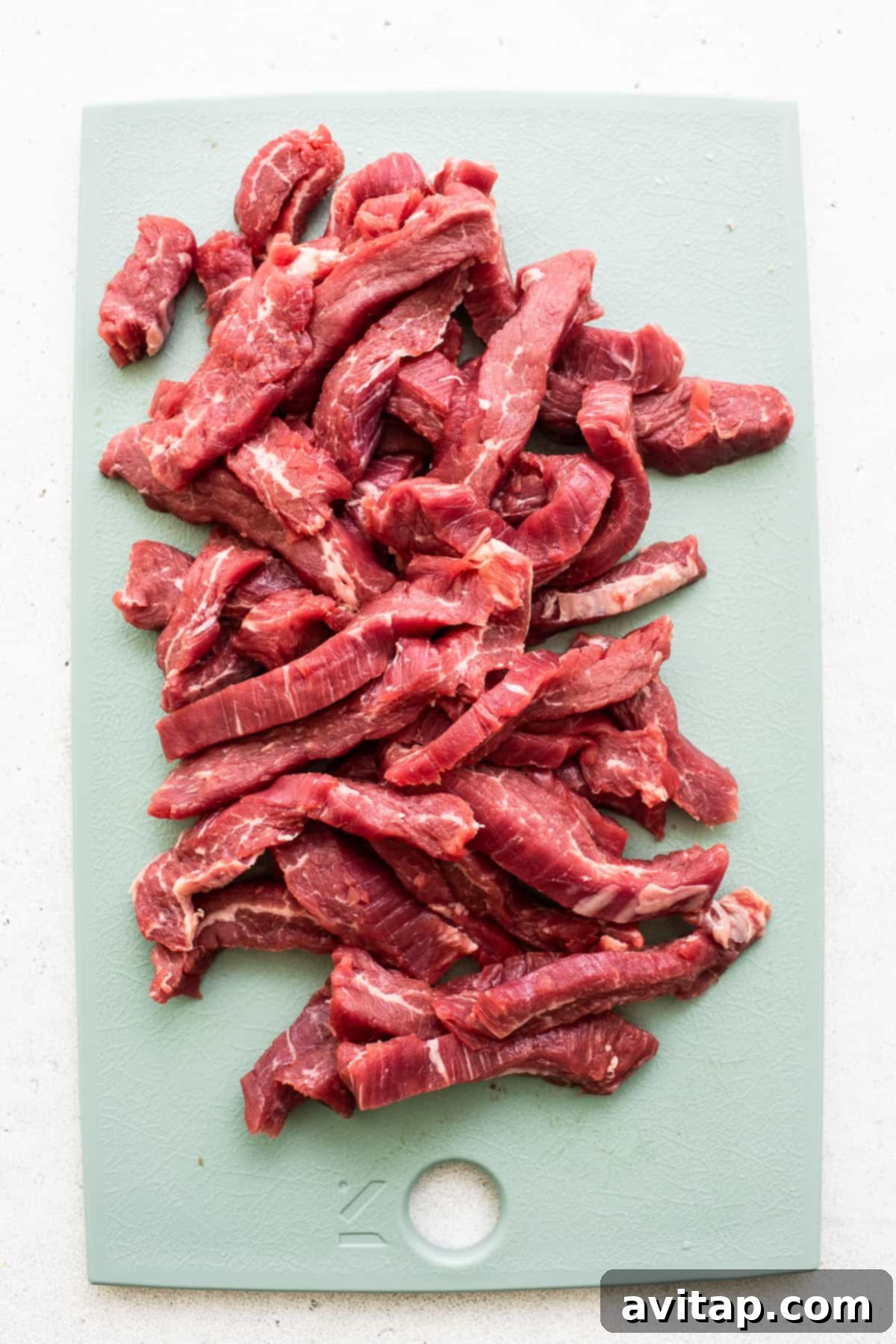 Thinly sliced flank steak on a cutting board, ready for stir-frying.