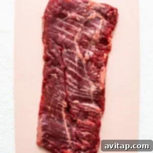 A piece of beef on a cutting board, being tenderized.