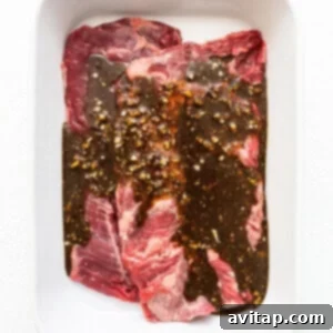 A white dish with a piece of beef in it, covered in marinade.