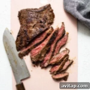 A piece of grilled steak on a pink cutting board, ready to be sliced.