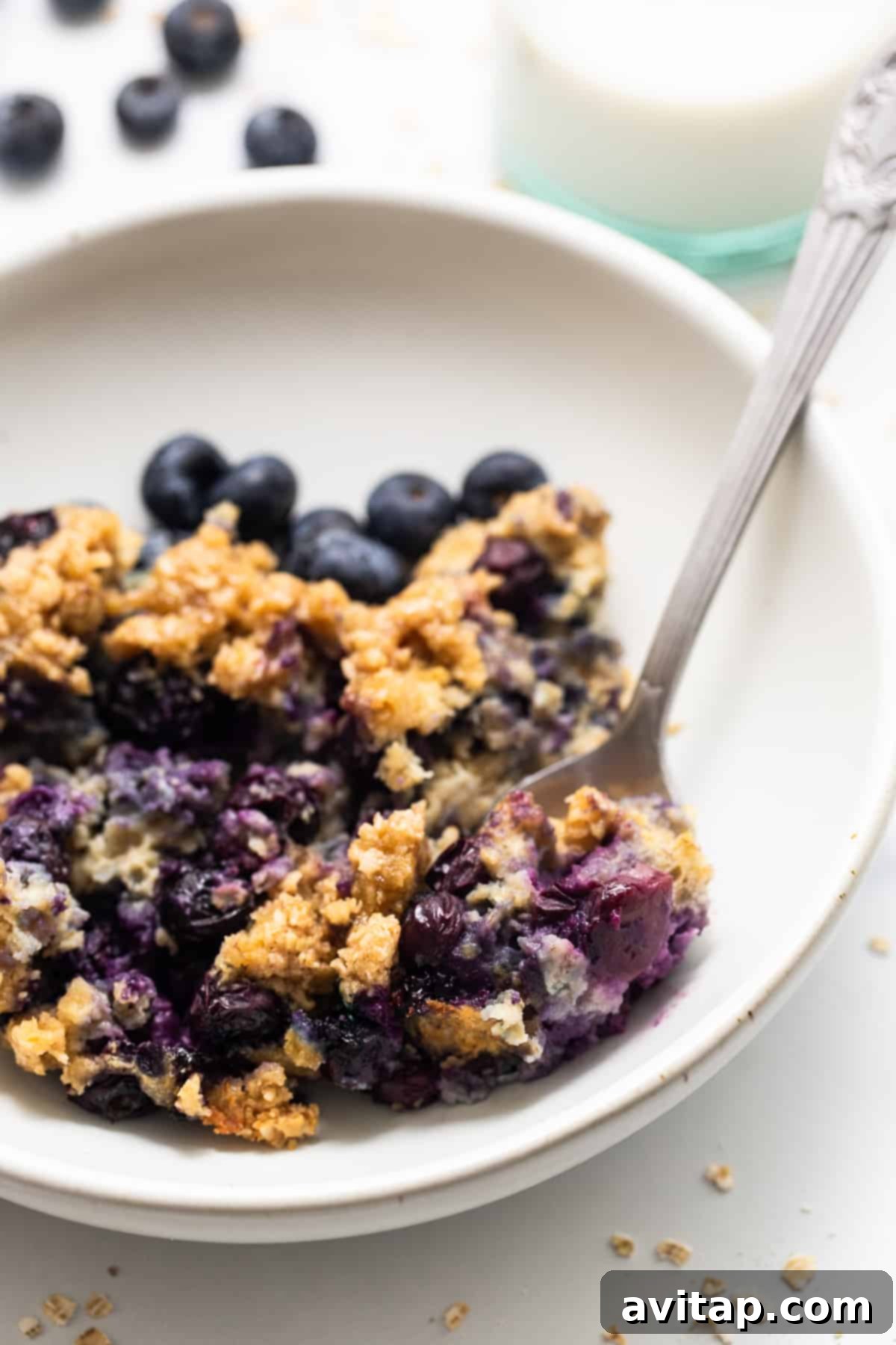 A warm bowl of blueberry muffin baked oatmeal with a spoon, ready to be enjoyed.