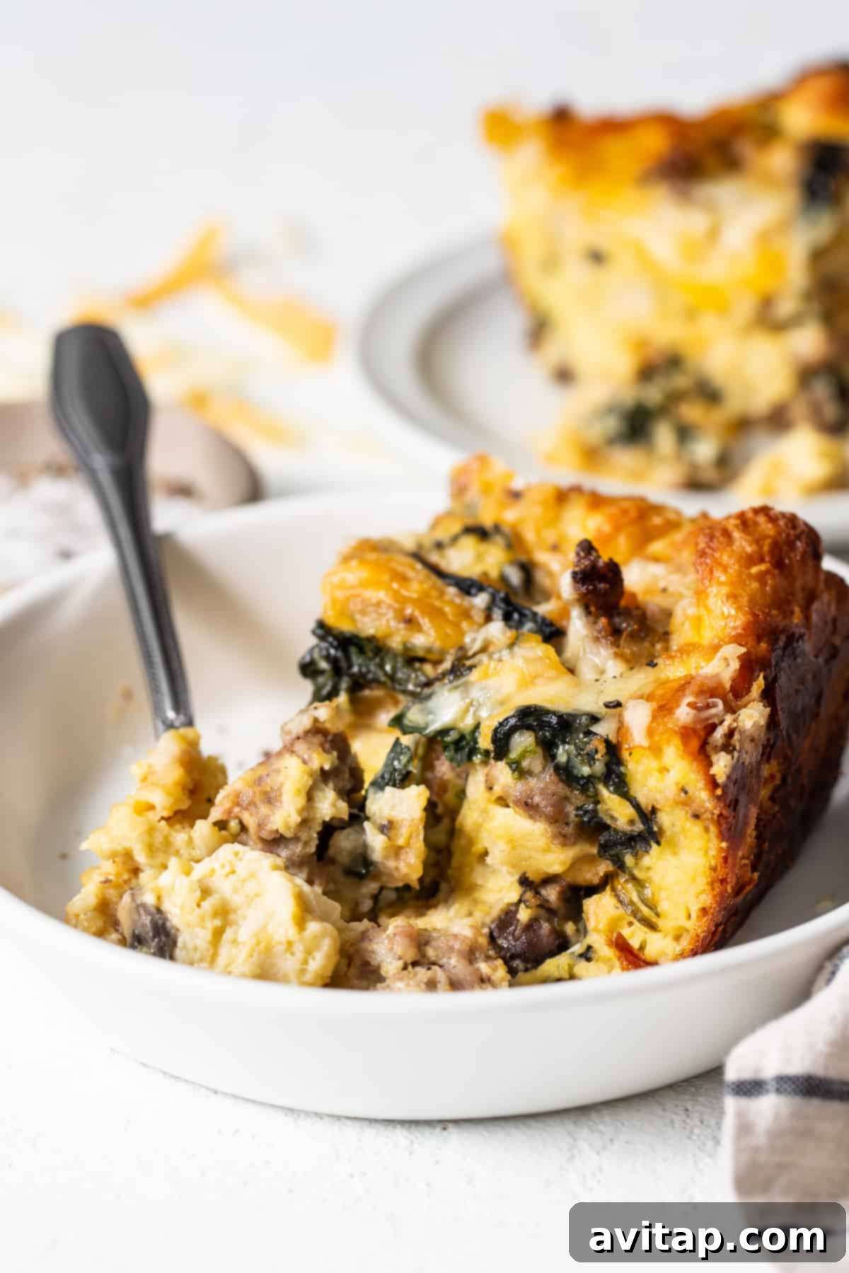 A delicious slice of classic breakfast strata on a white plate with a fork, ready to be enjoyed.
