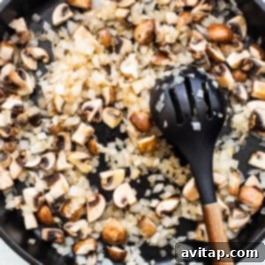 Mushrooms being sautéed in a skillet with a wooden spoon.