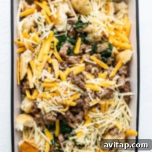 A casserole dish filled with layered meat, cheese, spinach, and bread, ready for the egg custard.