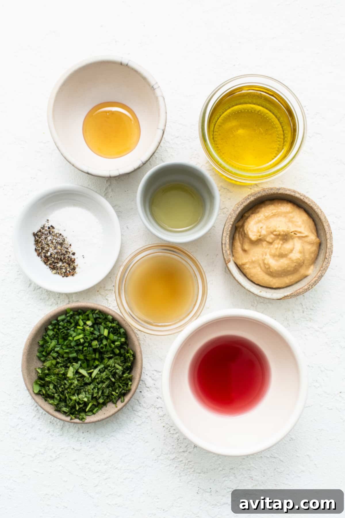 A collection of fresh ingredients laid out on a countertop, including hummus, herbs, olive oil, and lemons.