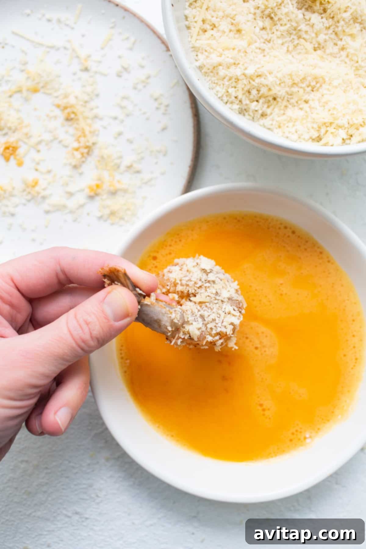 A close-up shot of panko-coated shrimp being dipped into an egg wash bowl, showcasing the breading process.
