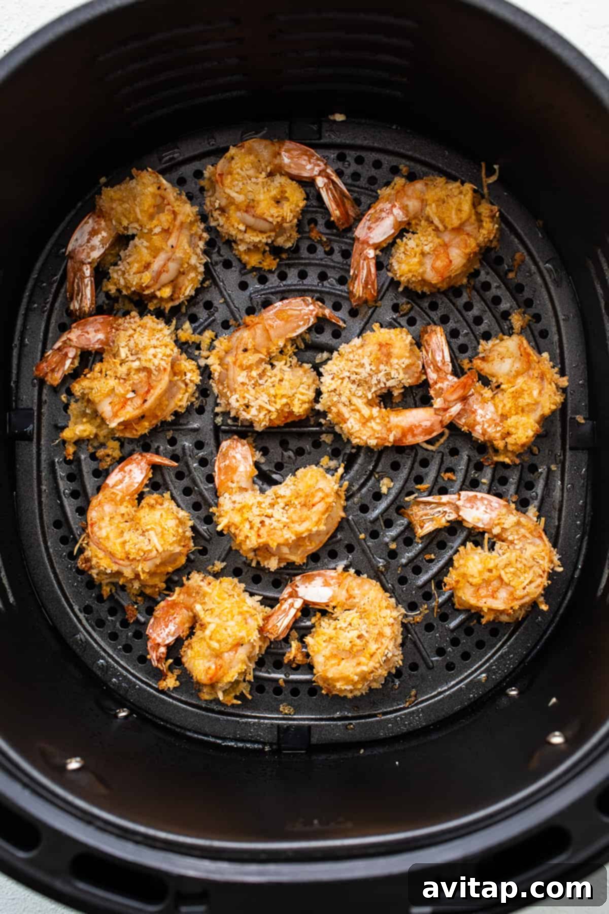 Perfectly cooked golden-brown shrimp resting in an air fryer basket after being air-fried.