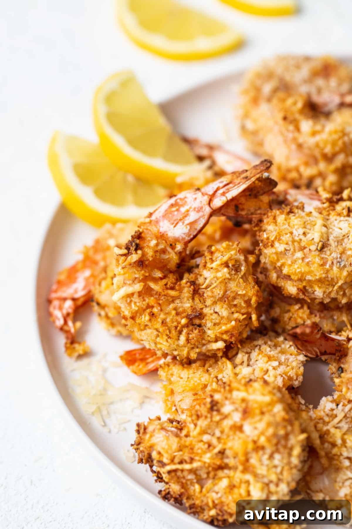 A plate of golden, crispy air fryer shrimp garnished with fresh parsley and lemon slices, ready to be enjoyed.