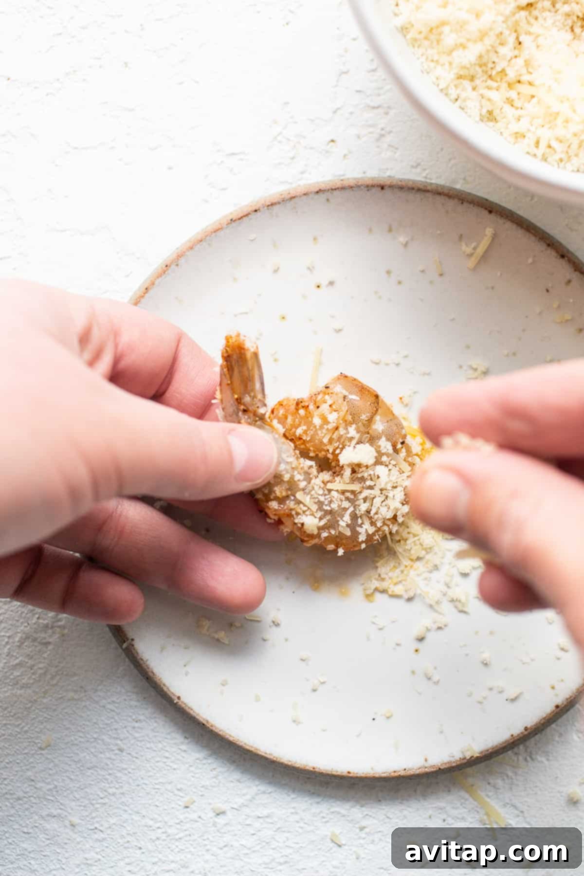 Shrimp being coated with a generous mixture of panko breadcrumbs and grated Parmesan cheese.