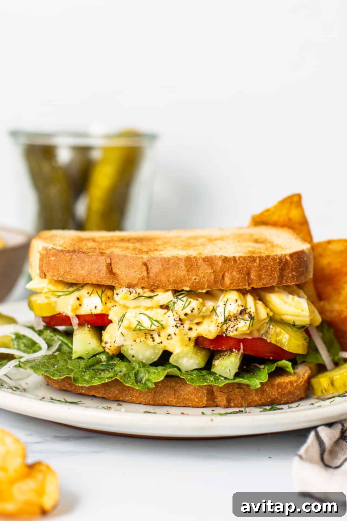 Classic Homemade Egg Salad Sandwich 2 A delicious homemade egg salad sandwich, sliced in half, on a white plate with a side of crispy chips.