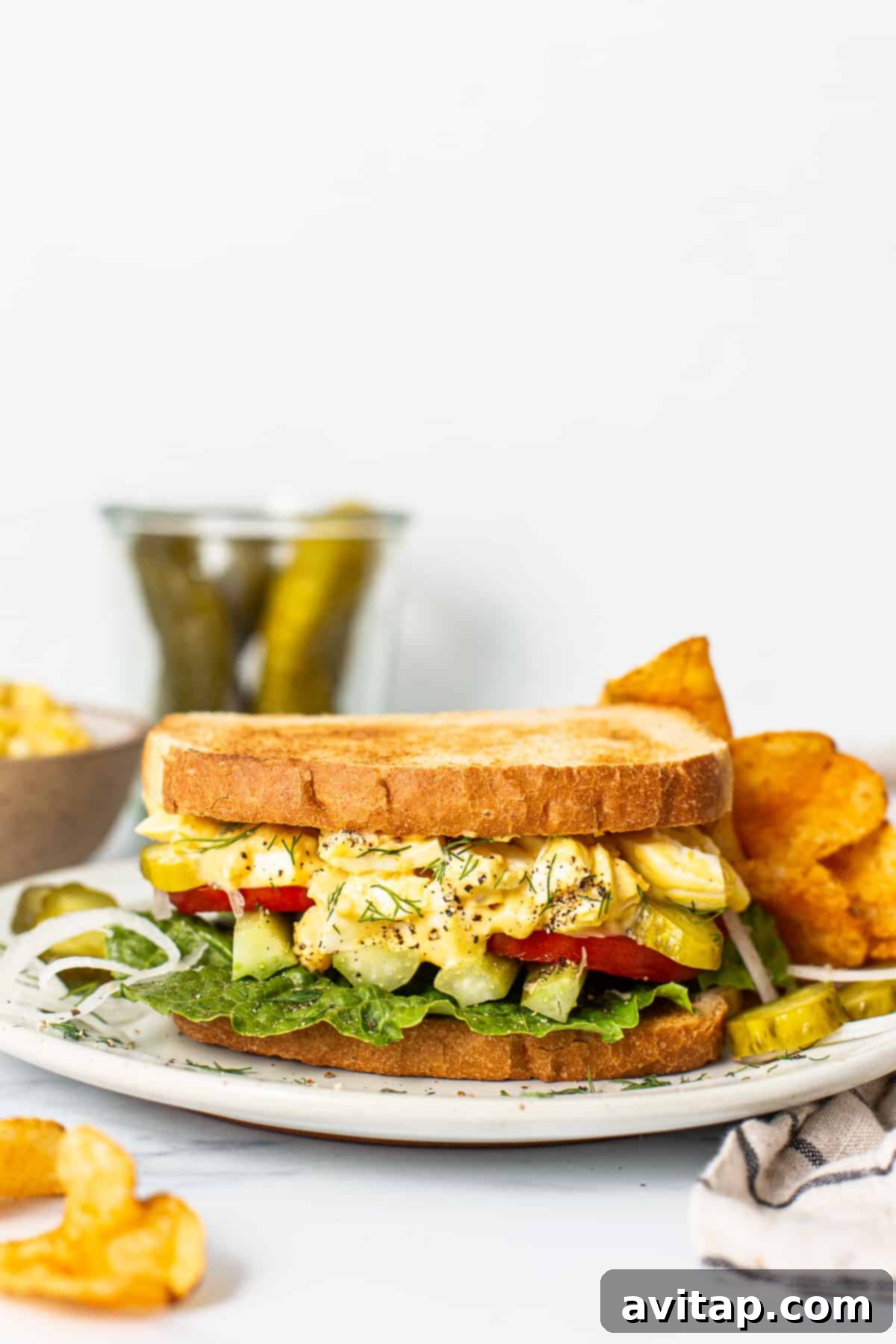 Classic Homemade Egg Salad Sandwich 6 A close-up of an egg salad sandwich on a plate, paired with crunchy kettle chips, ready for a delicious meal.