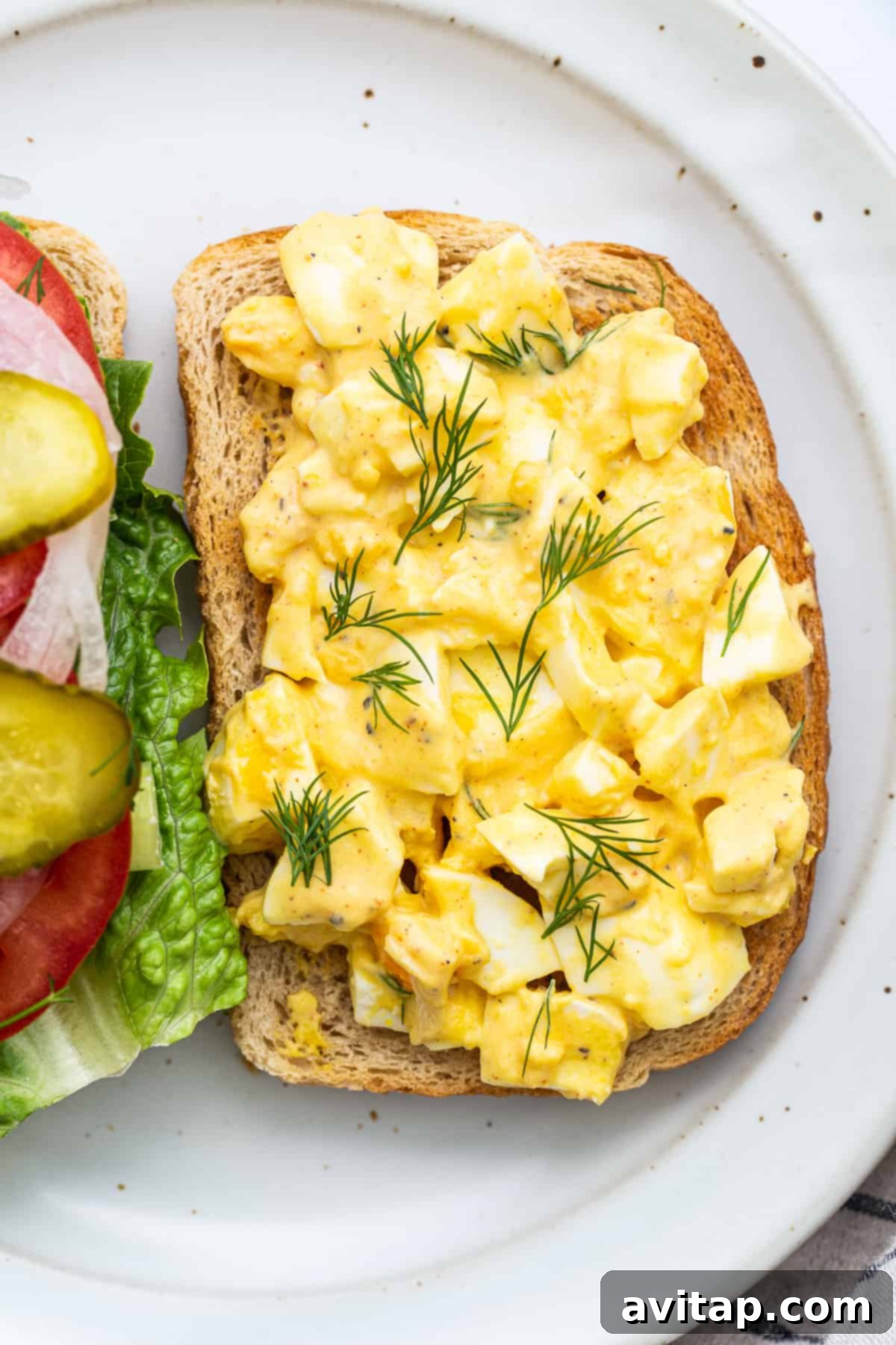 Classic Homemade Egg Salad Sandwich 5 Close-up shot of creamy egg salad generously sprinkled with fresh green dill, highlighting its vibrant freshness.