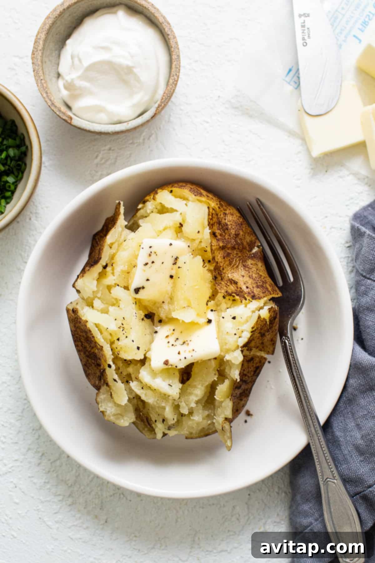 A perfectly cooked Instant Pot baked potato, split open and generously topped with melting butter, served in a simple bowl, ready to eat.