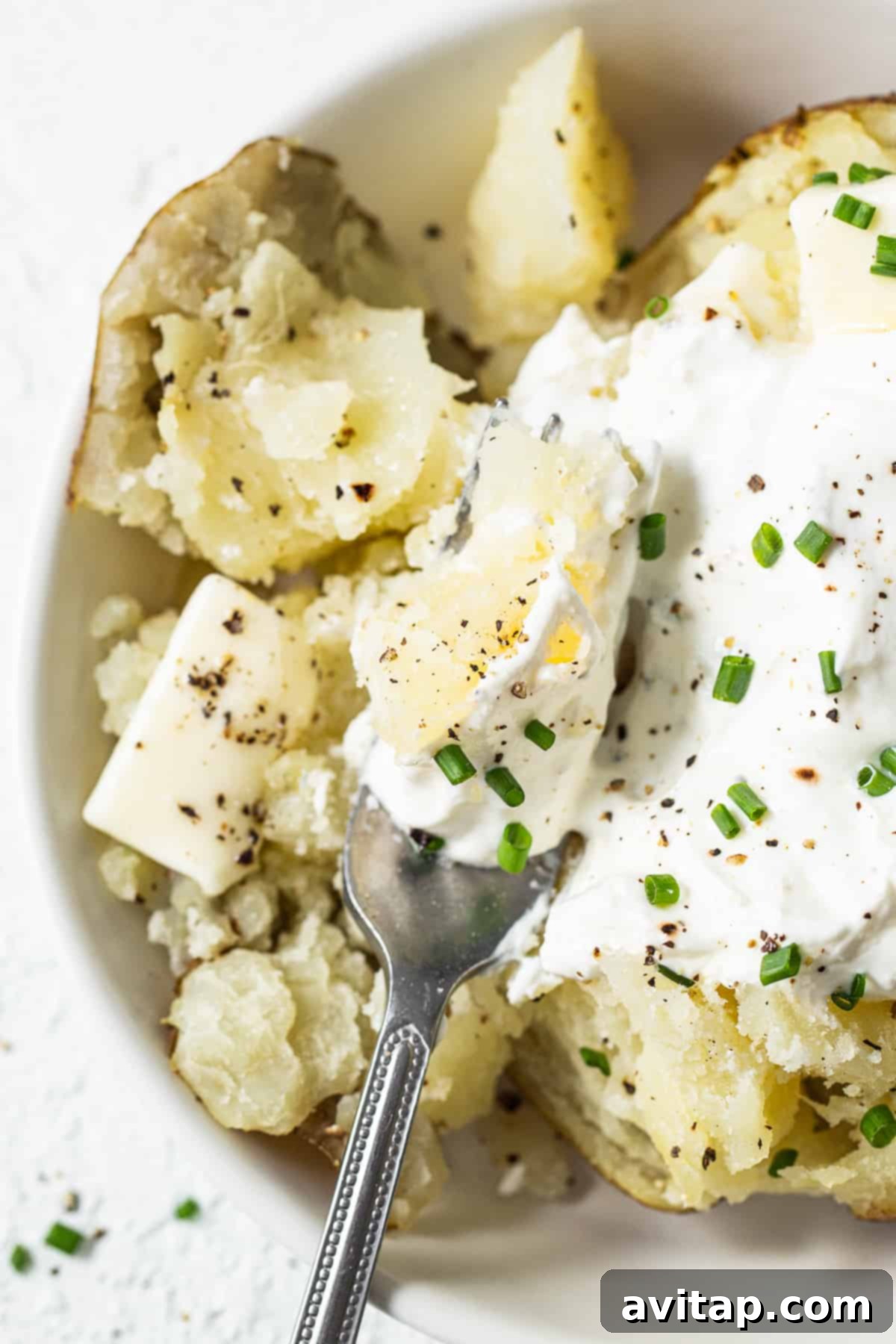 A close-up shot of a perfectly fluffed baked potato, demonstrating its soft, tender texture with a fork gently pulling apart the flesh.