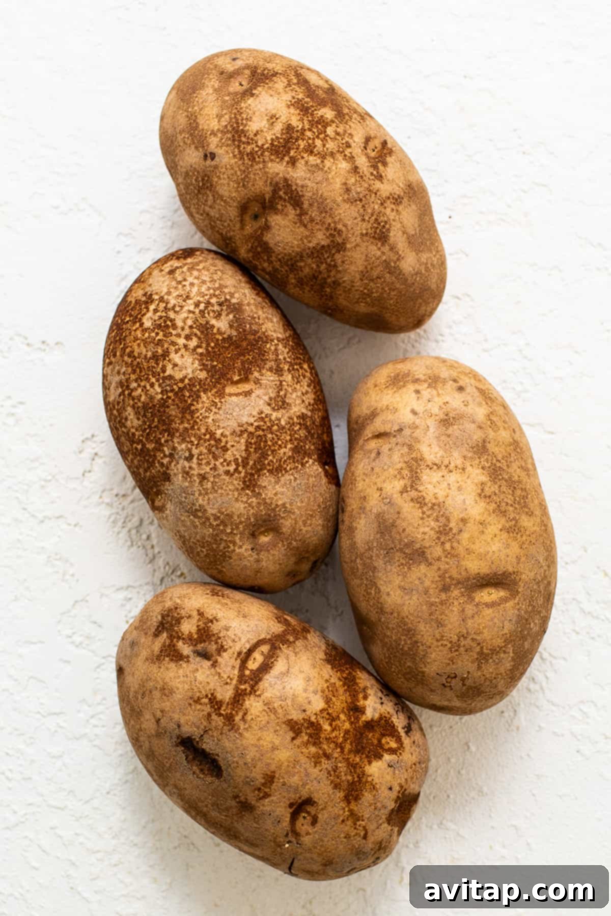 Fresh russet potatoes neatly arranged on a kitchen countertop, washed and ready for preparation.