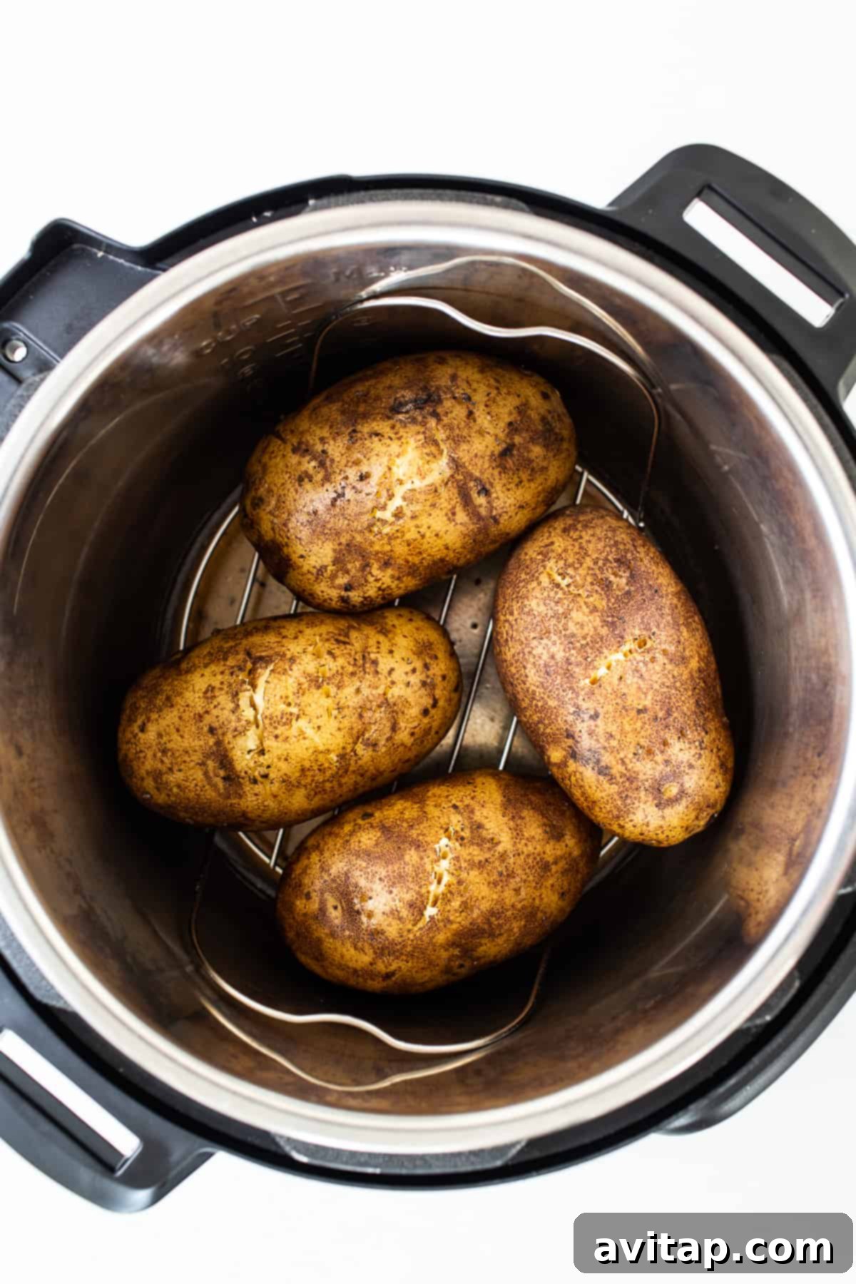 Several seasoned raw potatoes placed inside an Instant Pot on a metal rack, carefully arranged and ready for pressure cooking.