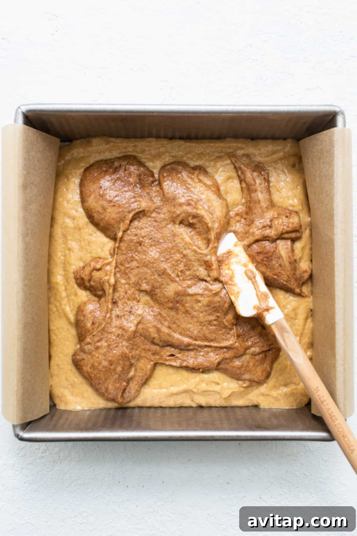 A baker carefully spreading the cinnamon layer into the coffee cake batter.