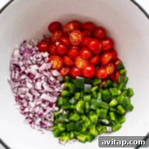 Fiesta Street Corn Chicken Salad 4 Diced vegetables including bright red cherry tomatoes, green bell peppers, and red onion marinating in a large bowl.