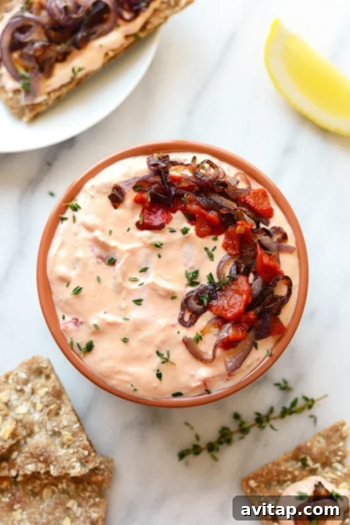 Smoky Red Pepper Chevre Dream 4 An overhead shot of the roasted red pepper and goat cheese dip in a white bowl, surrounded by various dippers like crackers and fresh vegetables.