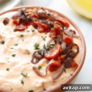 Smoky Red Pepper Chevre Dream 6 A bowl of roasted red pepper and goat cheese dip with onions and tomatoes, ready to be served.