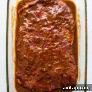 Ultimate Steak Fajita Marinade 6 A glass baking dish containing flank steak submerged in the green marinade.